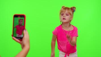 Happy little Caucasian kid girl blogger front of phone camera record enjoy dance content on green chroma key background. Social distance coronavirus pandemic concept. Freedom active lifestyle video