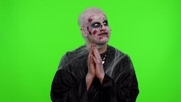 Sneaky cunning zombie man with makeup with wounds scars with tricky face gesticulating and scheming evil plan, thinking over devious villain idea, cunning cheats, jokes and pranks. Sinister dead guy video