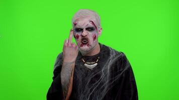 Aggressive crazy hooligan Halloween zombie man with makeup with wounds scars showing around his middle fingers, demonstrating protest with impolite rude gesture of disrespect, rejecting communication video