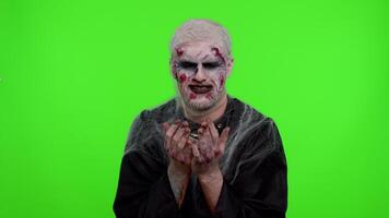 Upset disappointed zombie man with makeup with wounds scars wipes tears and cries from despair, being sad because of unfair things in chroma key studio. Sinister dead guy. Halloween, filming, staging video