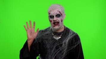 Creepy man with bloody scars face, Halloween zombie make-up. Scary wounded undead guy smiling friendly at camera and waving hands gesturing hello or goodbye, welcoming with hospitable expression video