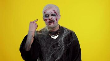 Aggressive crazy hooligan Halloween zombie man with makeup with wounds scars showing around his middle fingers, demonstrating protest with impolite rude gesture of disrespect, rejecting communication video