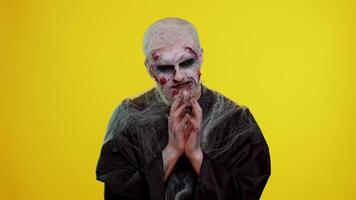 Sneaky cunning zombie man with makeup with wounds scars with tricky face gesticulating and scheming evil plan, thinking over devious villain idea, cunning cheats, jokes and pranks. Sinister dead guy video