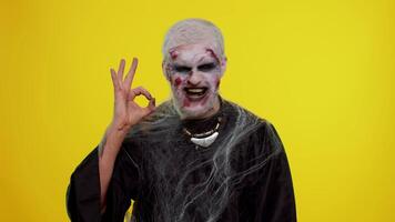 Creepy man with bloody scars face, Halloween stylish zombie make-up. Scary wounded undead guy looking approvingly at camera showing Ok gesture, like sign positive something good and smiles terribly video