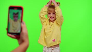 Cheerful funny little teen girl kid dancing at camera filming using phone at home on chroma key background. Schoolgirl child creating her trendy content on a mobile app to share on social media video