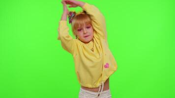 Happy little Caucasian kid girl blogger front of phone camera record enjoy dance content on green chroma key background. Social distance coronavirus pandemic concept. Freedom active lifestyle video