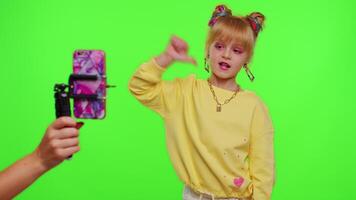 Young Blogger Concept. Cheerful teen school girl kid dancing at camera filming using phone at home on chroma key background, creating her trendy content on a mobile app to share on social media video