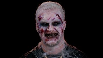 Sinister man with horrible scary Halloween zombie makeup in costume showing dirty teeth, looking ominous at camera trying to scare. Dead guy with wounded bloody scars face isolated on black background video