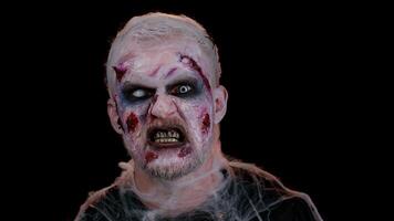 Unexpected appearance of frightening man with Halloween zombie bloody wounded make-up, trying to scare, face expressions. Horror theme. Sinister undead guy isolated on studio black wall background video