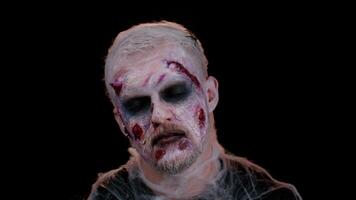 Unexpected appearance of sinister man with horrible scary Halloween zombie makeup making faces, looking ominous at camera, trying to scare. Dead guy with wounded bloody scars face. Black background video