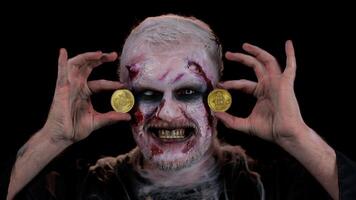 Zombie man with make-up with fake wounds scars showing golden bitcoins. Achievement career wealth, cryptocurrency investment, mining btc, future technology. Sinister dead guy. Halloween, filming video