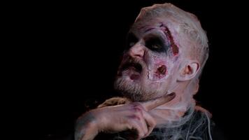 Sinister man with horrible scary Halloween zombie makeup in costume making faces, looking ominous at camera, showing kill gesture in police lights, trying to scare. Dead guy with wounded bloody face video