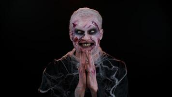 Sneaky cunning zombie man with makeup with wounds scars with tricky face gesticulating and scheming evil plan, thinking over devious villain idea, cunning cheats, jokes and pranks. Sinister dead guy video