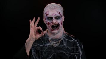 Creepy man with bloody scars face, Halloween stylish zombie make-up. Scary wounded undead guy looking approvingly at camera showing Ok gesture, like sign positive something good and smiles terribly video
