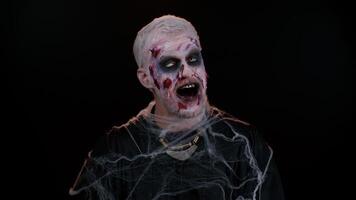 Creepy man with bloody scars face, Halloween zombie make-up. Scary wounded undead guy smiling friendly at camera and waving hands gesturing hello or goodbye, welcoming with hospitable expression video