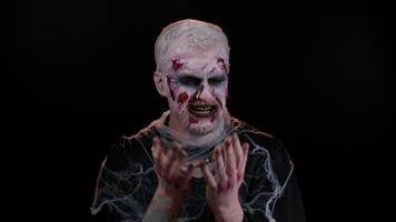 Upset disappointed zombie man with makeup with wounds scars wipes tears and cries from despair, being sad because of unfair things in dark studio room. Sinister dead guy. Halloween, filming, staging video