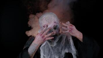 Creepy man with bloody scars face, Halloween stylish zombie make-up. Scary wounded undead guy looks at camera hiding through spider web, smiles terribly, scares. Thematic party. Sinister beast monster video