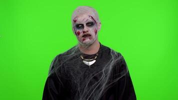 Sinister man Halloween crazy zombie with bloody wounded scars face trying to scare showing killing gesture, runs a finger along his neck isolated on chroma key. Horror theme of cosplay wounded undead video