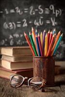 Colorful Pencils and Books Beside Glasses on Wooden Table in Study With Math Equations in Background photo