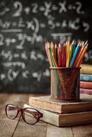 Colorful Pencils and Books Beside Glasses on Wooden Table in Study With Math Equations in Background. photo