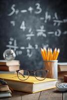 Colorful Pencils and Glasses on a Desk in a Classroom Filled With Books and Chalkboard Equations. photo