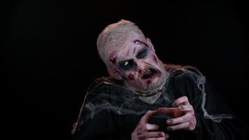 Sinister man with horrible scary Halloween zombie makeup in convulsions making faces, looking ominous, trying to scare. Dead guy with wounded bloody scars face isolated against black wall background video