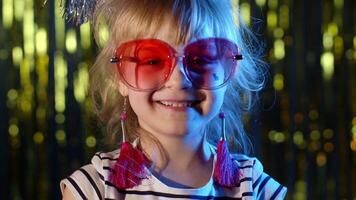 Portrait of trendy stylish girl looking at camera, smiling. Elegant child kid in neon lighting posing at disco party cyberpunk club. Futuristic hipster teenager children making faces, fooling around video