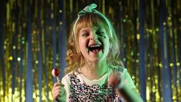 Trendy stylish girl with lollipop candy looking at camera smiling, screaming, shouting. Child kid in neon lights posing at disco club. Futuristic hipster teenager children making faces, fooling around video