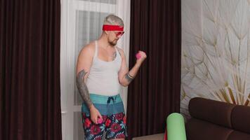 Stylish hipster man blogger trainer recording sport weightlifting online exercises with dumbbells vlog at home. Funny bodybuilder sportsman guy couch showing biceps. Joke, comical meme, parody, humor video