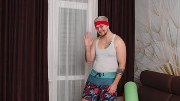 Hello or bye. Sportsman retro guy in funny sport clothes waving greeting with hand, showing thumbs up, smiling at home. Portrait of fat bearded man hipster of 80s. Joke, comical, meme, parody, humor video