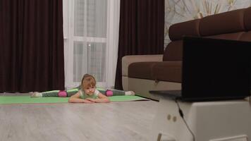 Child kid girl doing gymnastics fitness stretching twine workout at home. Fitness online program on laptop computer. Remote distance education, tutorial, training, family quarantine isolation video