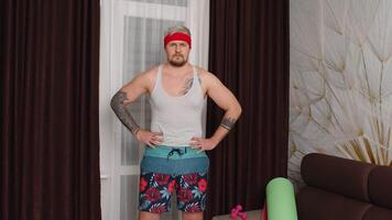 Funny man athlete sportsman guy from the 80's with beard makes workout stretching at home. Portrait of young stylish hipster man practicing sport, having fun, fooling around. Fitness parody concept video
