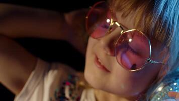 Elegant child kid in neon lighting posing at disco party cyberpunk club. Portrait of trendy stylish girl looking at camera, smiling. Futuristic hipster teenager children making faces, fooling around video
