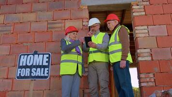 Diverse team of specialists taking near modern house. Real estate building project with senior civil engineer, architect, general worker discussing planning, development details on digital tablet video
