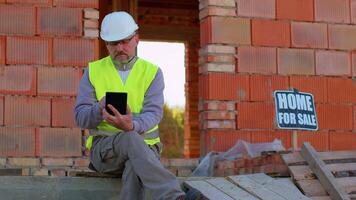 Male construction engineer. Architect with a digital tablet computer at construction site. Man worker foreman looking analyzing blueprints, building house place on background. Construction concept video
