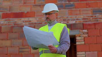 Confident engineer architect wearing a safety hardhat and vest working repairing on construction site of house. Business, real estate, investment. Foreman worker builder designer analyzes blueprints video