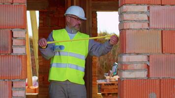 Civil engineer architect specialist conducting measurements with a tape measure at construction site. House on background. Developer builder in helmet inspecting building. Real estate home project video