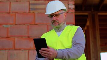 Civil engineer architect specialist operate with digital tablet to control working at construction site. House on background. Developer builder in helmet inspecting building. Real estate home project video