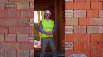 Confident Caucasian engineer architect wearing safety hardhat and vest conducting measurements with a tape measure on construction site of house. Business, real estate. Foreman worker builder designer video