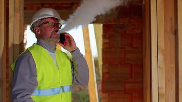 Professional builder engineer architect talking on mobile phone to control working at construction site. Foreman worker wearing hard hat and vest at building house. Business, real estate, investment video