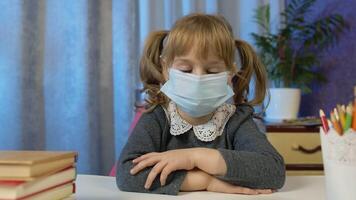 Child girl in medical mask studying homework during online lesson at home. Looking at web camera. E-learning, webinar. Online distance education for children caused by coronavirus pandemia quarantine video