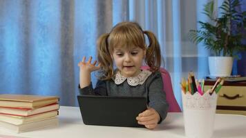 Child schoolgirl learns lessons with teacher being at home sitting at table using digital tablet computer. Portrait of a kid pupil girl distance education. Studying on coronavirus quarantine lockdown video