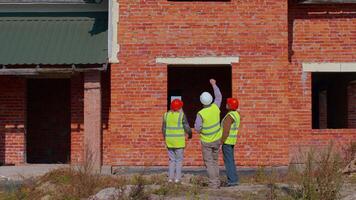 Diverse team of specialists taking near modern house. Real estate building project with senior civil engineer, architect, general worker discussing planning, development details. Purchasing, renting video