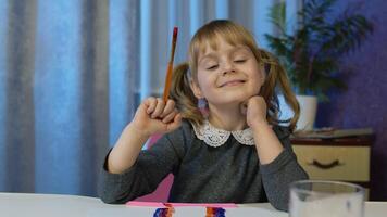Back to school, online learning, distance lesson, pupil education at home. Child girl kid enthusiastically drawing with brushes, paints with laptop computer at home, looking at camera, smiling pupil video