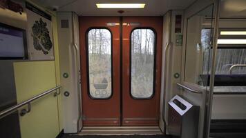 Interior of Swiss double-decker train showing orange automatic doors with windows, handrails and digital display. Train moving through countryside, highlighting modern public transport infrastructure. video