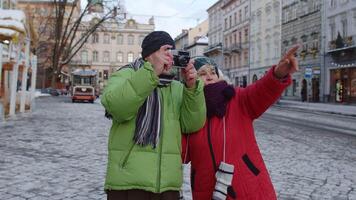 mayor esposa y marido turistas tomando foto imágenes en retro cámara, caminando, gesticulando en invierno ciudad calle en lviv, Ucrania. familia vacaciones ocupaciones y fotografía. vida después Jubilación video