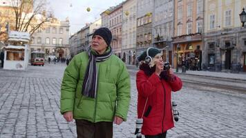 elegante mayor mayor Pareja turistas abuela y abuelo de viaje, tomando foto imágenes en retro cámara en invierno ciudad calle. encantador maduro pensionistas familia vacaciones Navidad Días festivos video