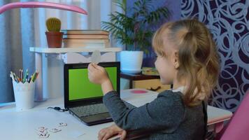 Online kids distance remote education, children e-learning lesson. Child girl pupil doing school homework with teacher using laptop computer with green screen at home. call by webcam on internet video
