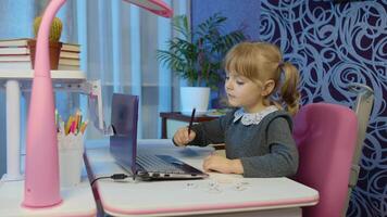 Little child girl doing school homework using laptop at home. Online e-learning, children pupil distance education lesson, technology for kids. Typing on computer and writes in notebook. 6k downscale video