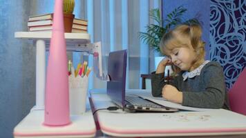 Preschool child girl distance online learning at home. Bored kid listening audio lesson studying at table using digital laptop computer doing homework. Children remote education on covid-19 quarantine video